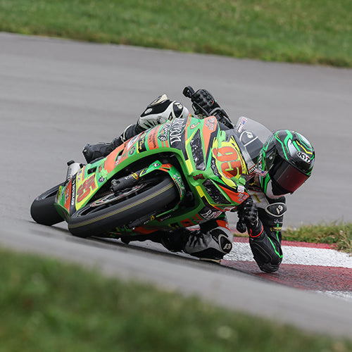 Matthew Chapin at full lean, dragging knee and elbow through a corner at a race track with his KYT KX-1 Race GP motorcycle helmet